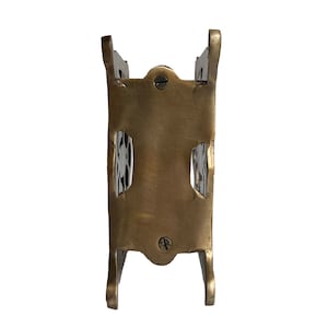 May include: A vintage brass-toned metal object with a rectangular body and curved legs. The object has two rectangular cutouts and is secured with screws. The overall design suggests a small decorative holder or stand.