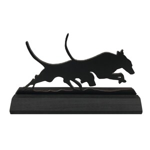 May include: Black silhouette of a dog running, mounted on a black wooden base.