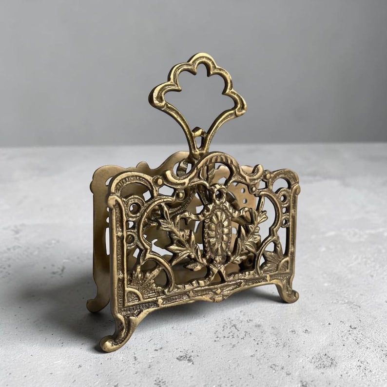 May include: Ornate brass letter holder with a decorative handle. The vintage desk organizer features intricate floral and scrollwork designs. The brass finish gives it an antique look, perfect for adding a touch of elegance to any workspace.