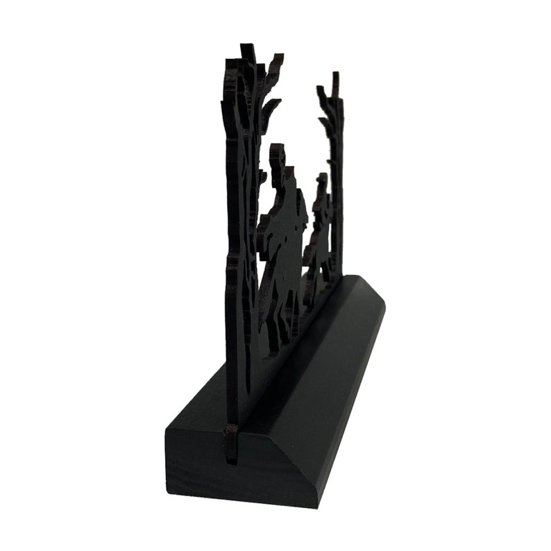 May include: Black wooden silhouette of three people walking through a forest. The silhouette is mounted on a black wooden base.