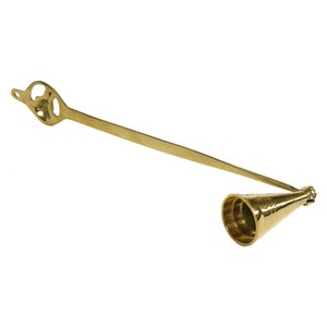 May include: A gold metal candle snuffer with a long handle and a cone-shaped tip. The handle has a decorative design.