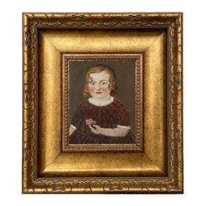 May include: An antique portrait of a child in a gold ornate frame. The child is wearing a red and black plaid dress and holding a small pink flower. The frame has a gold finish with detailed carvings.