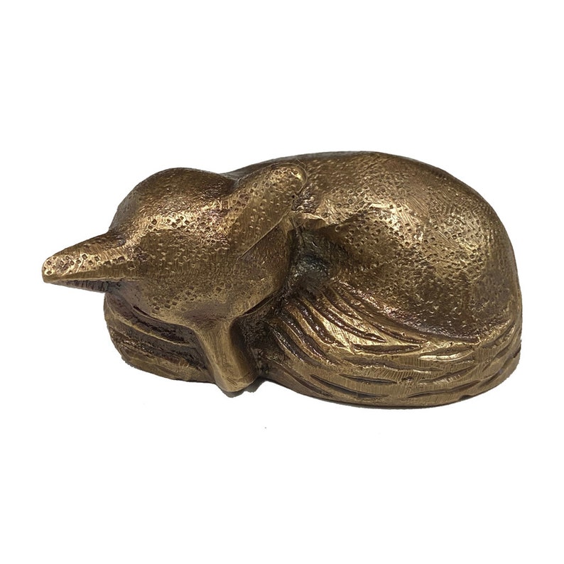 May include: A small, bronze sculpture of a sleeping fox. The fox is curled up with its head resting on its paws. The sculpture has a textured surface and is made in a realistic style.