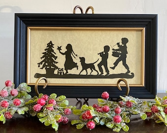 May include: Black silhouette of children and a dog walking past a Christmas tree. The image is framed in black with a gold inner frame.