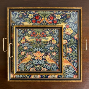 K&ouml;nnte beinhalten: Zwei dekorative Tabletts mit einem Blumen- und Vogelmuster. Das gr&ouml;&szlig;ere Tablett hat goldene Griffe und einen goldenen Rahmen. Das kleinere Tablett ist in das gr&ouml;&szlig;ere eingenistet. Die Tabletts haben einen dunkelblauen Hintergrund mit roten Erdbeeren, gelben V&ouml;geln und gr&uuml;nen Bl&auml;ttern.