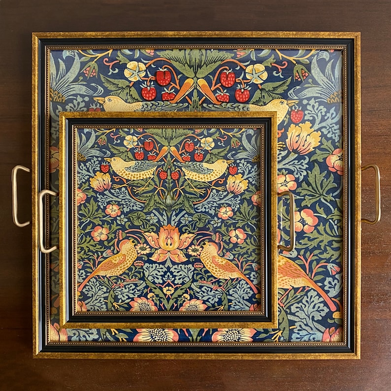 K&ouml;nnte beinhalten: Zwei dekorative Tabletts mit einem Blumen- und Vogelmuster. Das gr&ouml;&szlig;ere Tablett hat goldene Griffe und einen goldenen Rahmen. Das kleinere Tablett ist in das gr&ouml;&szlig;ere eingenistet. Die Tabletts haben einen dunkelblauen Hintergrund mit roten Erdbeeren, gelben V&ouml;geln und gr&uuml;nen Bl&auml;ttern.
