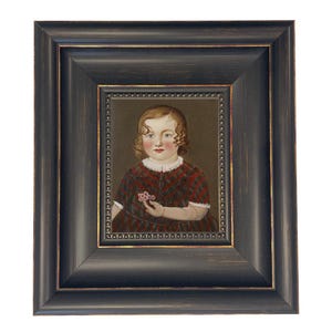 May include: A framed portrait of a young child with curly hair, wearing a red and brown plaid dress, holding a small flower. The portrait is set within a dark, ornate wooden frame with gold accents, creating a vintage aesthetic.