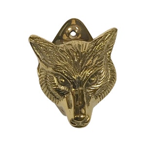 May include: A gold-toned brass fox head bottle opener. The fox's head is detailed with fur and has a realistic expression. The bottle opener is mounted on a wall.