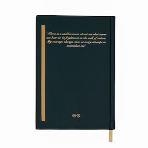 May include: A dark teal journal with gold text and a gold ribbon bookmark. The text reads, "There is a stubbornness about me that never can bear to be frightened at the will of others. My courage always rises at every attempt to intimidate me."