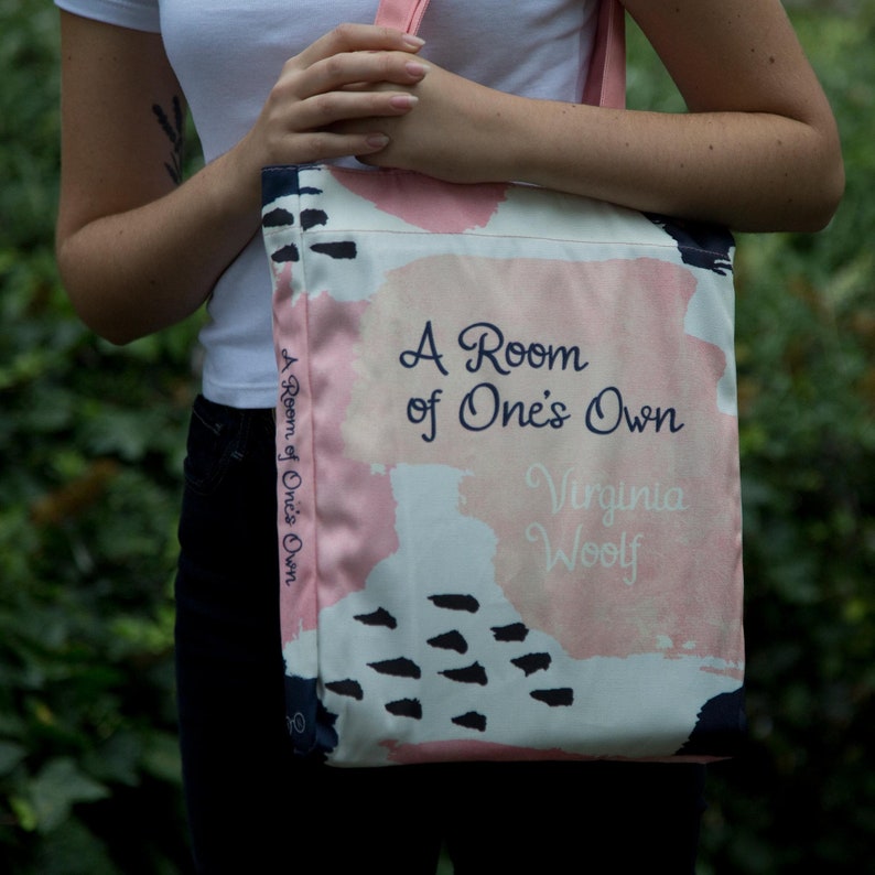 May include: A pink and white tote bag with black abstract designs. The bag features the text "A Room of One's Own" and "Virginia Woolf".