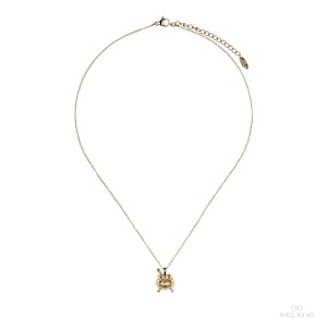Puede incluir: Un collar dorado con un peque&ntilde;o colgante. El colgante tiene un dise&ntilde;o detallado con un elemento central y adornos. La cadena es fina y ajustable, con un cierre de broche.