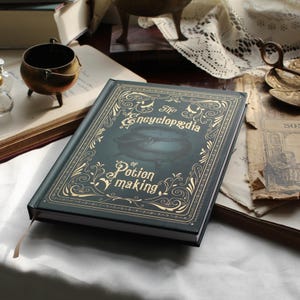 May include: A dark green book titled "The Encyclop&aelig;dia of Potion Making" with gold lettering and illustrations. The book has a decorative cover with a cauldron image. A bronze cauldron and open books are in the background.
