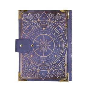 May include: A purple leather-bound journal with gold accents and a decorative design featuring a star with an eye in the center. The design includes a circle of symbols and a floral pattern.