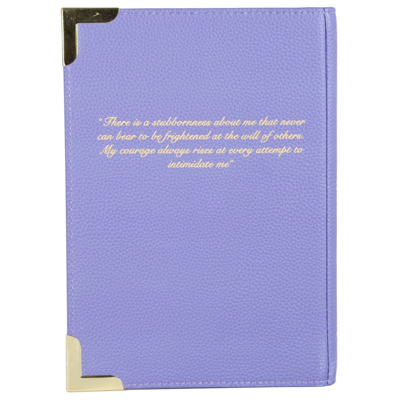 May include: A purple leather-bound journal with gold corners and a quote in gold lettering that reads: "There is a stubbornness about me that never can bear to be frightened at the will of others. My courage always rises at every attempt to intimidate me."