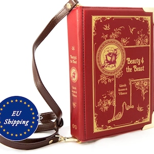 Könnte beinhalten: Eine rote Clutch-Tasche aus Kunstleder in Buchform mit einem goldfarbenen Verschluss und einem verstellbaren braunen Riemen. Die Vorderseite der Tasche zeigt ein goldfarbenes Design mit dem Titel "Die Schöne und das Biest" und einer Rosenillustration.