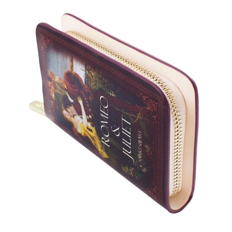 May include: A burgundy wallet with the cover art of Shakespeare's "Romeo & Juliet." It has a gold zip, cream interior, and the title text. The wallet is designed to look like a book.