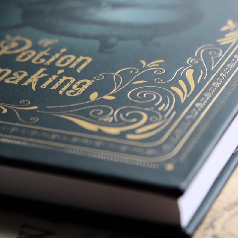 May include: A close-up of a dark teal book with gold lettering and decorative flourishes. The text on the cover reads "Potion Making". The book's edges are white, and the cover has a textured appearance.