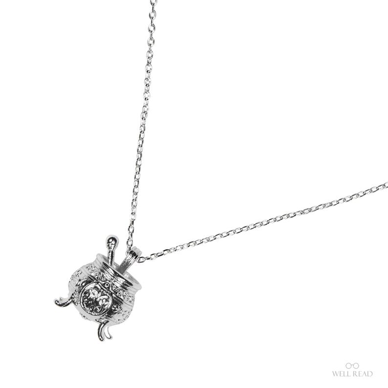 Puede incluir: Un collar plateado con un colgante de caldero. El colgante presenta detalles intrincados y una piedra similar a un cristal. La cadena est&aacute; hecha de peque&ntilde;os eslabones. El dise&ntilde;o es caprichoso y elegante. Ideal para regalo.