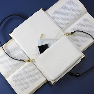 May include: A white leather crossbody bag with a gold zipper and a black strap. The bag is open and a phone and a small white pouch are inside.