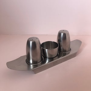 Puede incluir: Un juego de salero y pimentero de plata con un soporte para condimentos a juego. El juego está hecho de acero inoxidable y tiene un diseño moderno.