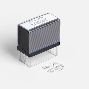 May include: A black and clear address stamp with the text "the future Smiths, 123 Main Street, Franklin, TN 37043" in a handwritten style. The stamp is shown with a printed impression of the address on a white surface.