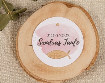 May include: A round, white tag with a pink watercolour design and the text "22.05.2022 Sandra's Taufe" on a wooden slice.