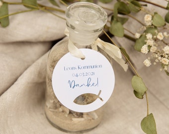 May include: A small glass bottle filled with sand and a white tag tied around the neck. The tag has a blue fish cutout and the text "Leon's Kommunion 04.03.2021 Danke!"