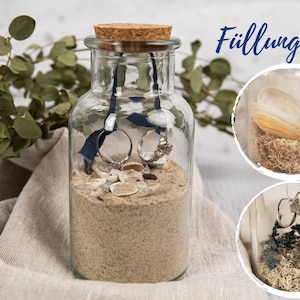 May include: A clear glass jar with a cork lid filled with sand, seashells, and two rings. The jar is sitting on a light brown fabric surface. The text "F&uuml;llungen" is visible in the upper right corner of the image.