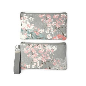 May include: Two gray zippered pouches with a floral print. The top pouch is a clutch and the bottom pouch has a gray strap.