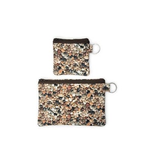 May include: Two rectangular pouches featuring a realistic print of smooth, multi-colored river stones in shades of gray, brown, tan, and white. Each pouch has a dark brown zipper closure along the top edge and a metal ring attached to the side.