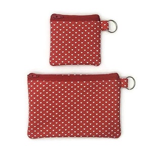 May include: Two red zippered pouches with white heart patterns. The smaller pouch has a key ring attached.