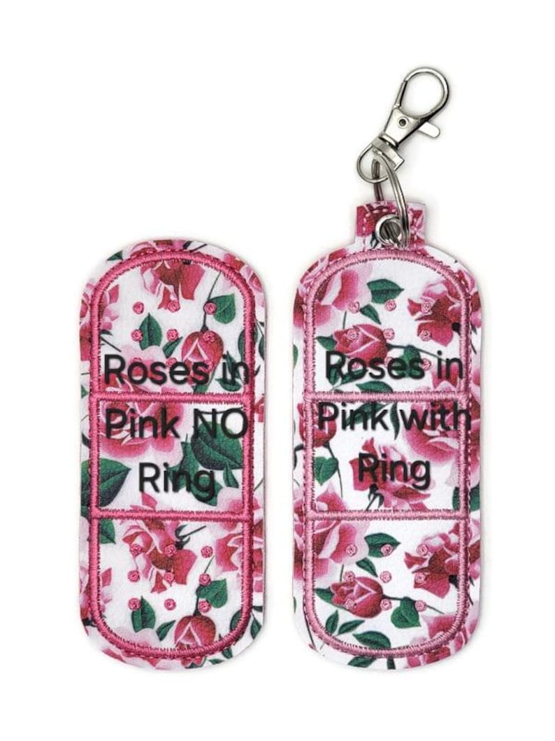 May include: Two pink and white floral patterned fabric keychains with a silver metal clasp. The keychains are shaped like a band-aid and have the text "Roses in Pink NO Ring" and "Roses in Pink with Ring" embroidered on them.