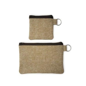 May include: Two zippered pouches made of brown linen fabric with brown zipper pulls and silver key rings. The smaller pouch is on top of the larger pouch.