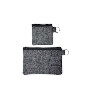 May include: Two zippered pouches made from a grey and black patterned fabric. The smaller pouch has a silver ring attached to the zipper pull. The larger pouch has a silver ring attached to the zipper pull on the right side.