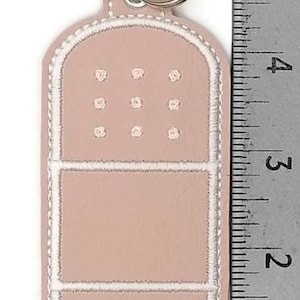 May include: A pink leather keychain shaped like a bandage with white stitching. The keychain has a silver metal ring and a silver metal clasp.