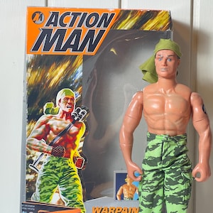 May include: An Action Man figure, Warpain, stands in front of its box. The figure is shirtless, wearing green camouflage pants and a green head covering. The box features the Action Man logo and an illustration of the figure.