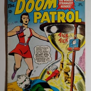 Può includere: Una copertina di fumetto vintage di "The Doom Patrol" con una donna in abito rosso e bianco, un personaggio con la faccia a orologio e una clessidra con un orologio che ticchetta. La copertina ha uno sfondo blu e il testo "The World's Strangest Heroes!"