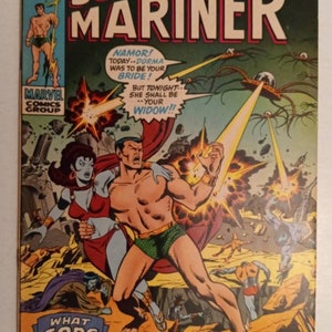 Könnte beinhalten: Vintage Sub-Mariner Comic-Cover. Das Cover zeigt Namor, eine muskulöse Figur in grünen Badehosen, mit einer Frau in roter Kleidung. Explosionen und Sprechblasen tragen zur actionreichen Szene bei. Das Marvel Comics Group-Logo ist sichtbar.