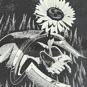 May include: A rectangular black fabric patch featuring a white screen-printed illustration of a sunflower growing out of a metallic helmet. The design is enclosed within a white chain-link border and includes a small circular icon at the top center.