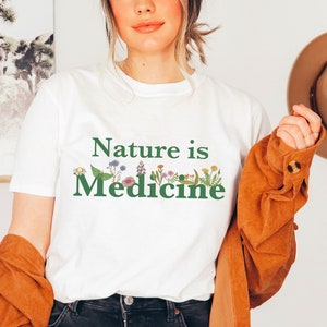 May include: White t-shirt with a green graphic that says "Nature is Medicine" with a line of colorful flowers and leaves.