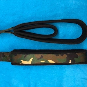 May include: A black padded dog leash and collar set. The collar features a camouflage pattern with a metal D-ring. The leash has a padded handle and a metal clasp. The set is designed for pet owners.