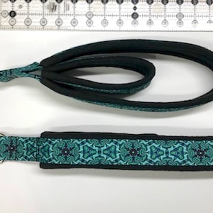 May include: A teal and black dog collar with a geometric pattern. The collar has a metal D-ring.