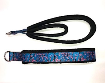 May include: A black and blue dog collar with a pink floral pattern. The collar has a padded lining and a metal D-ring.