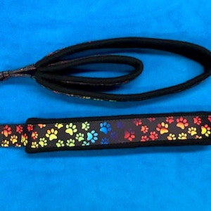May include: A black dog leash with a rainbow paw print pattern. The leash has a loop handle and a metal clip.