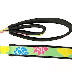 May include: A green, black, and yellow dog collar with a floral print. The collar has a black fleece lining and a metal D-ring.
