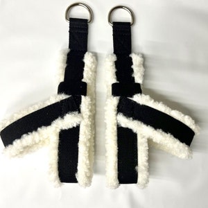 以下が含まれることがあります： 上部に銀色の金属ループが付いた、白くてふわふわの裏地が付いた黒と白のストラップが2本です