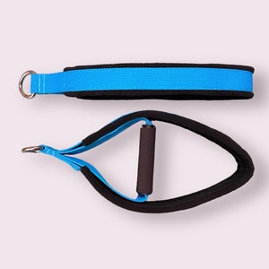 Puede incluir: Una correa de ejercicio azul y negra con un mango acolchado. La correa tiene un anillo de metal en un extremo y un mango acolchado en el otro.