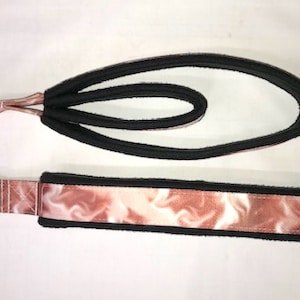 May include: A pink and white marbled dog leash with black edging and a silver metal clip. The leash is made of two separate pieces, one with a loop and one with a handle.