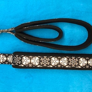May include: A black and white patterned dog leash with a silver metal clasp. The leash is made of a soft, flexible material and has a loop for attaching to a collar.