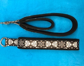 May include: A black and white patterned dog leash with a silver metal clasp. The leash is made of a soft, flexible material and has a loop for attaching to a collar.